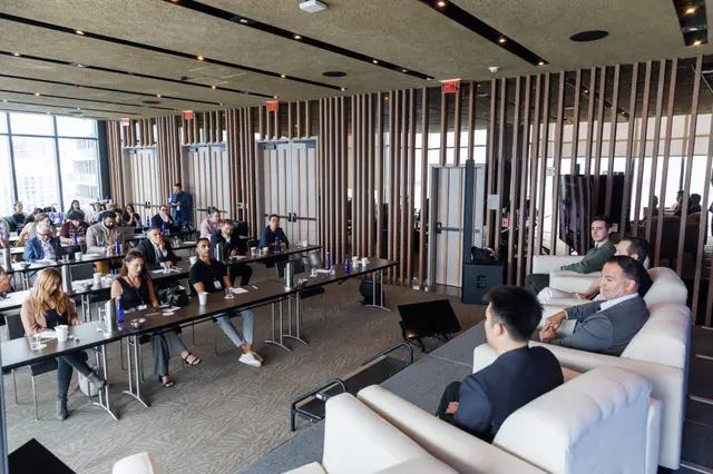Attendees seated along the windowed room with the city beyond